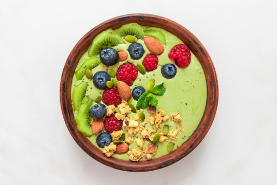 matcha tea green smoothie bowl with fresh berries, nuts, seeds and homemade granola for healthy vegan diet breakfast