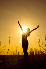 A young happy girl stands with open arms against the sun rays on the top of the mountain among the plants. Vertical orientation of the image