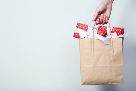 Female Hand Holding Shopping Bag With Gift Boxes On Grey Background