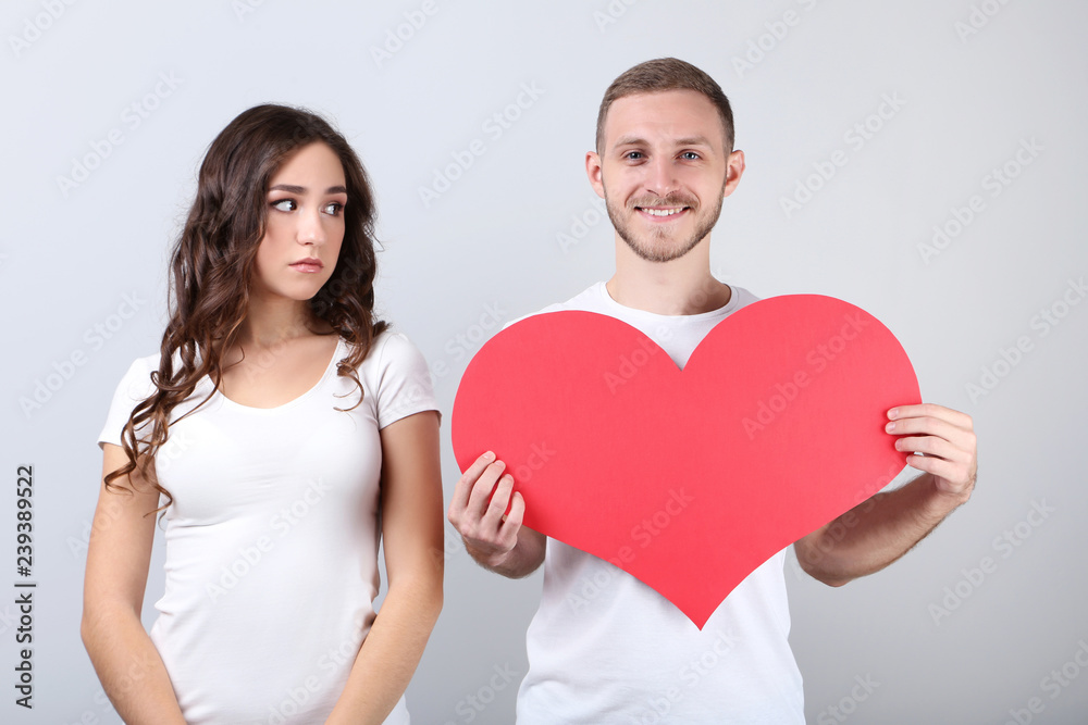 Wall mural beautiful young couple holding red paper heart on grey background