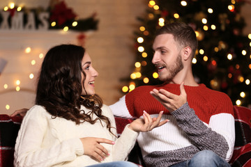 Happy young couple sitting at home near christmas tree