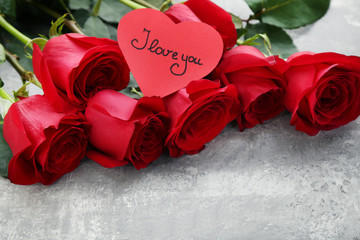 Bouquet of red roses with inscription I love you on grey wooden table