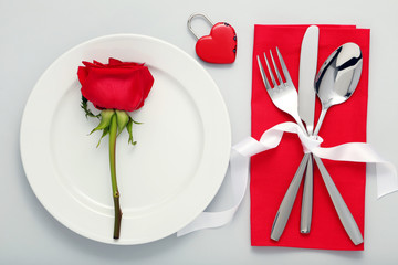 Kitchen cutlery with red rose in white plate on grey background