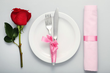 Kitchen cutlery in white plate with red rose and napkin on grey background