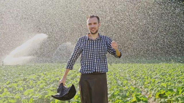Tired farmer takes off hat and raises hands up during irrigation of plantation