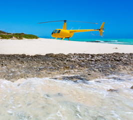 A yellow helicopter landed on idyllic empty sandy beach of remote island, azure turquoise blue lagoon in background, West Coast barrier reef, Coral sea, New Caledonia, Melanesia, South Pacific Ocean. © Dmitry