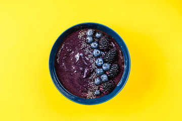 Plate with colorful acai smoothie seeing from above yellow background