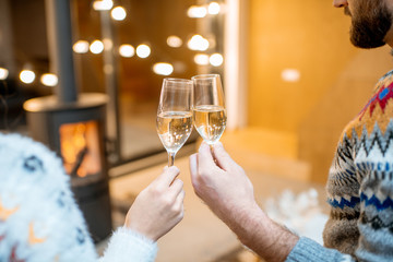 Clinking glasses with sparkling wine celebrating winter holidays at home with fireplace