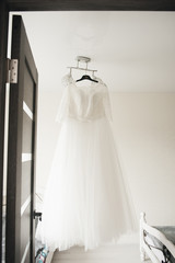 The bride's wedding dress hangs on a chandelier in a bright room