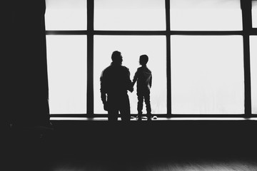 Silhouettes dads and sons standing near the window. Black and white photography