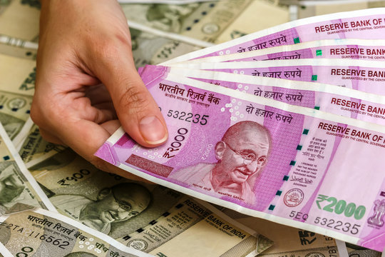 Close up view of woman's hands holding brand new indian 2000 rupees banknotes. 500 rupee banknotes in background.