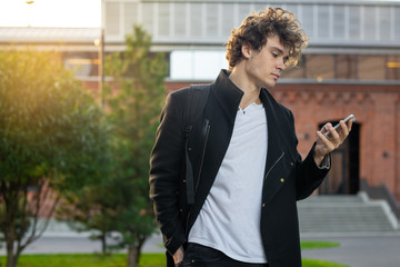 Man in black coat looking at mobile phone screen at cityscape urban background.