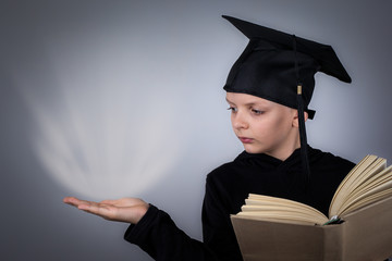 Student or pupil with black graduate hat reading opened shool book, hand showing something