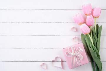 Valentines day and love concept. Pink paper hearts with gift box and tulips with ribbon on white wooden background.