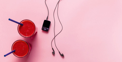 banner of red fresh fruit smoothies, mp3 player with headphones and black sneakers on a pink background. concept of youth, music, sport and health
