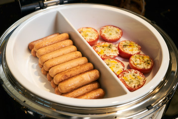 Tomato gratin and beef sausages in pan on electric kitchen stove