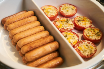 Tomato gratin and beef sausages in pan on electric kitchen stove