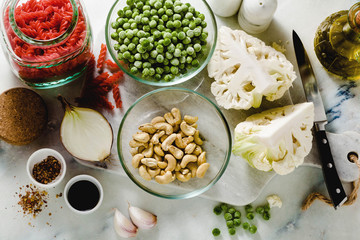 fresh ingredients for a gluten-free red lentil pasta with cauliflower and green peas with olive oil and spices on the marble table . healthy vegan cuisine