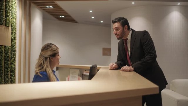Happy business man arriving at front office desk for meeting with customer, financial consultant in corporate reception to meet businessman. Manager talking to woman working as secretary