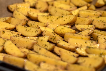 Kartoffelspalten mit Öl und Kräutern auf einem Backblech fertig um in den Ofen geschoben zu werden