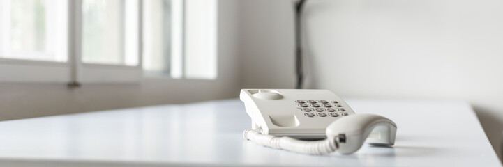 Wide view image of white landline telephone with handset off line