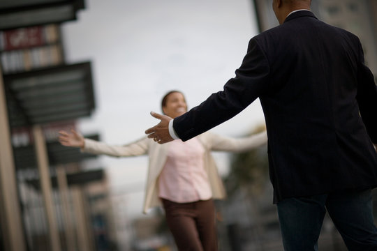 Man walking towards a woman with his arms out in an inner city street.
