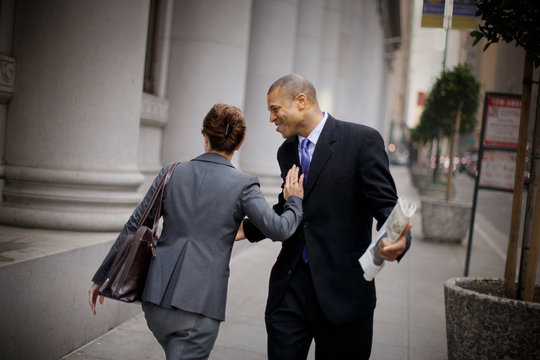Mid-adult businessman laughing while being pushed aside by a female colleague on an inner city sidewalk.