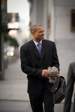 Smiling mid-adult businessman carrying a newspaper and briefcase while crossing a street in the city.