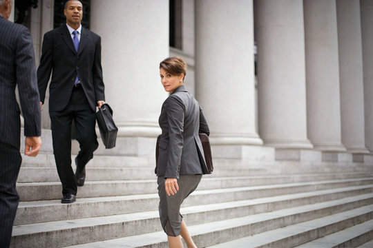 Portrait of a mid-adult businesswoman looking over her shoulder as she walks up the steps of a large building  the city.