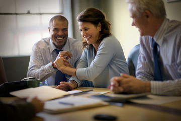 Mid-adult business woman laughing with two male colleagues in a board room.