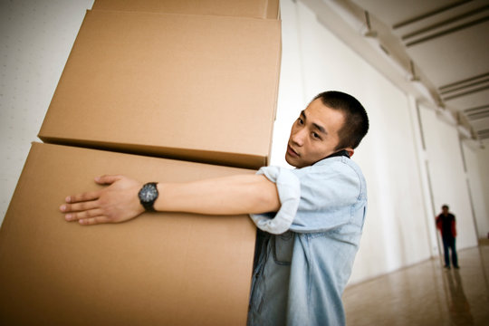 Young adult man carrying boxes and talking on  a cellphone in a building.