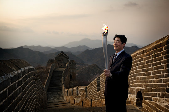 Mid-adult man carrying an Olympic torch along the Great Wall of China.