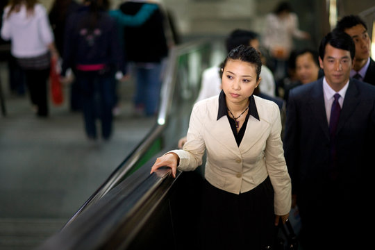 Young adult business woman using an escalator with colleagues.