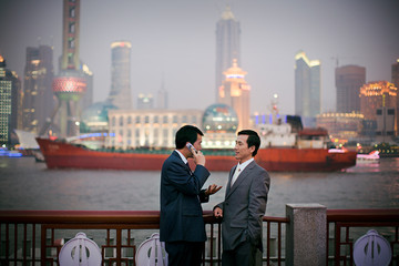 Young adult businessman talking on a cellphone while with a mid-adult male colleague in the city.