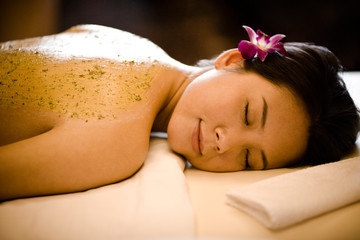 Young woman with closed eyes lying on her front with an exfoliant scrub smeared on her bare back.