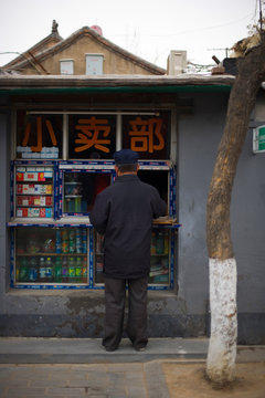 Male man standing outside a small shop on a street.