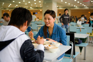Teenage girl sitting with a friend eating lunch.