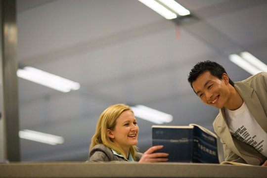 Mid-adult female teacher showing a teenage male student a book.