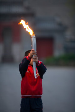 Young boy carrying an Olympic torch in a park.