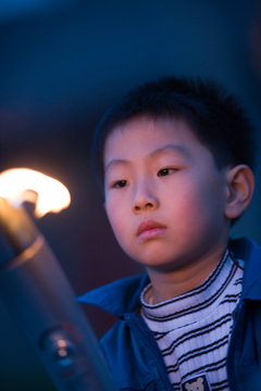 Young boy carrying an Olympic torch in a park.