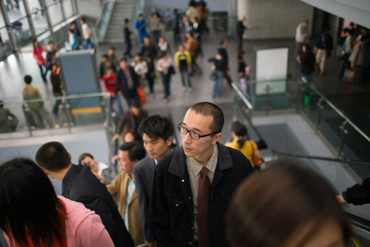 Young adult man going up an escalator with a group of people.