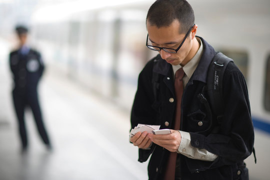 Young adult businessman looking through tickets on a train platform.