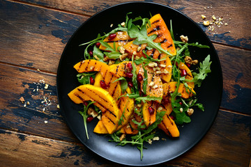 Grilled pumpking warm salad with arugula, walnuts and pomegranate seeds.Top view with copy space.