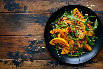 Grilled pumpking warm salad with arugula, walnuts and pomegranate seeds.Top view with copy space.