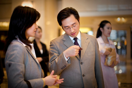 Young adult businessman standing with a mid-adult female colleague looking at a card in a lobby.