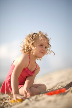 Young girl sitting on the beach in a bathing suit.