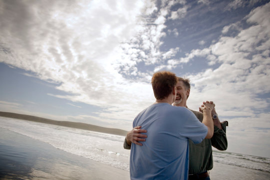 Homosexual male couple dancing together on a beach.