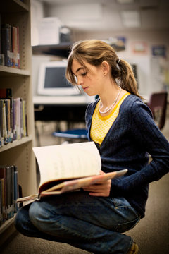 Teenage girl looking at books in a school library.