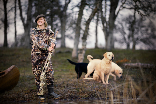 Young adult woman duck shooting with her dogs by a lake.