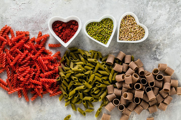 multicolor gluten-free pasta with ingredients in bowls in the form of hearts from which it is made on a stone table